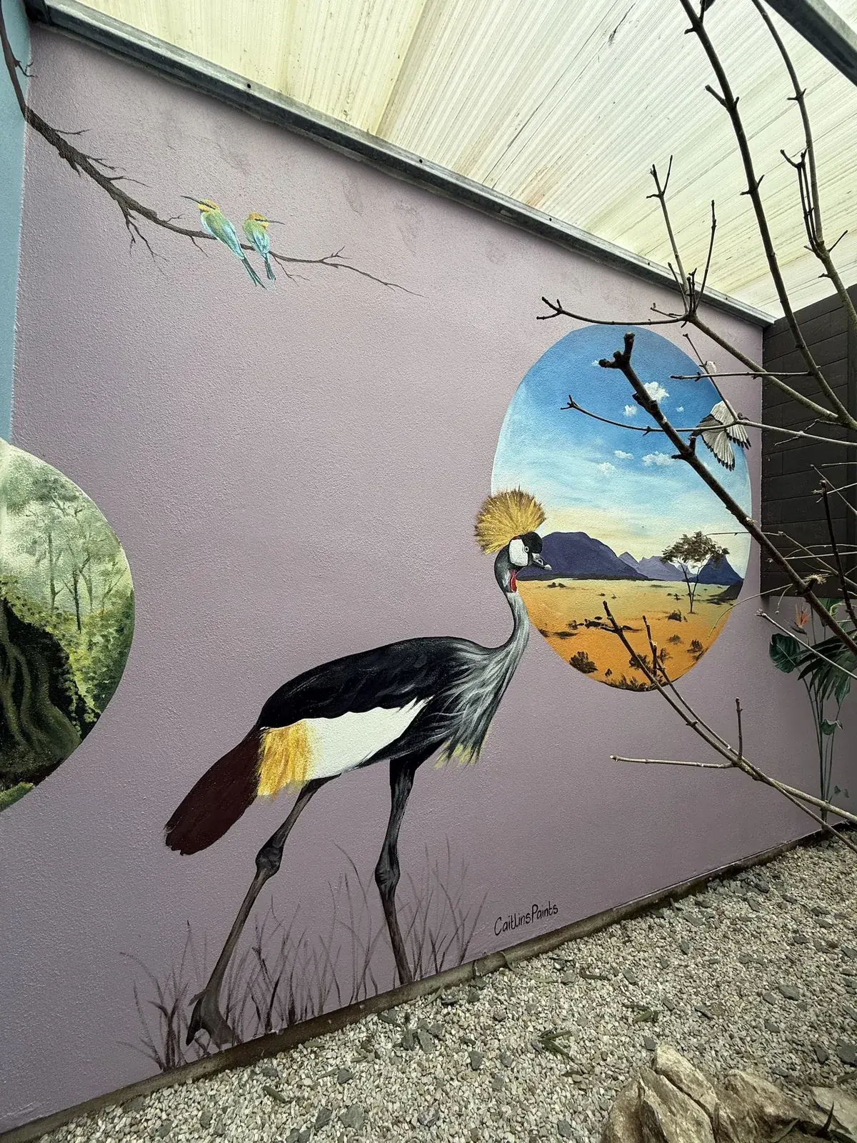 A grey crowned crane and savanna scene painted across a lilac courtyard wall