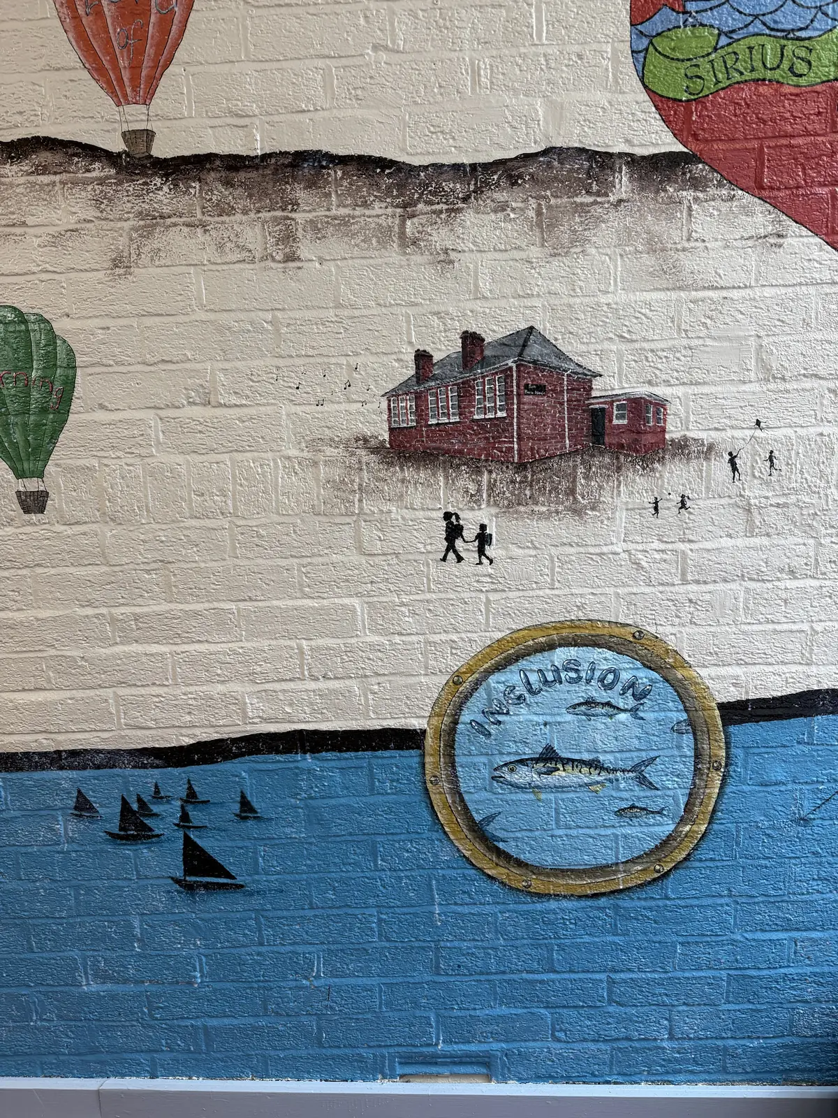 A school corridor mural — the old red-brick schoolhouse above a painted harbour, with the Inclusion porthole below the waterline