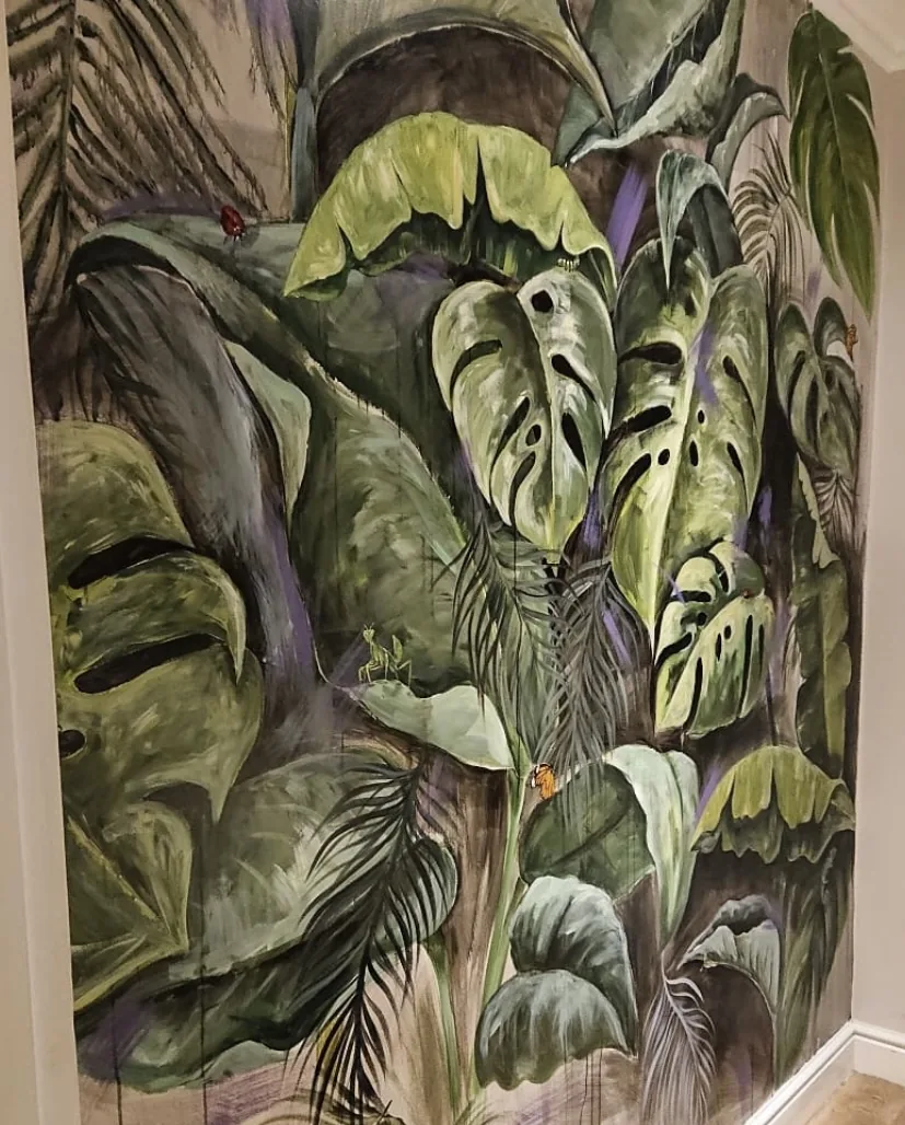 A dense painted jungle of monstera and banana leaves filling a cloakroom wall