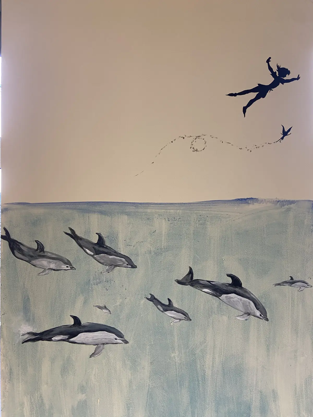 Dolphins swimming beneath the surface with Peter Pan in silhouette above